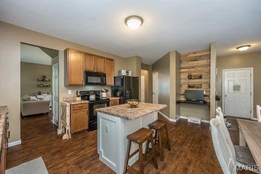 538 Springhurst Pkwy, Ofallon, MO 63368 - kitchen with black appliances, a kitchen breakfast bar, dark wood-type flooring, a center island, and baseboards