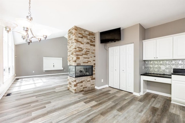 3 Wedgewood Ct, Edwardsville, IL 62025 - unfurnished living room with light wood-type flooring, a chandelier, a stone fireplace, baseboards, and an office area