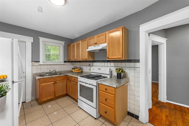 7348 Grand Dr, Pagedale, MO 63133 - kitchen with under cabinet range hood, white appliances, tasteful backsplash, a sink, and light countertops
