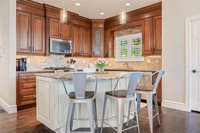 5360 Tower Hill Ct, Weldon Spring, MO 63304 - kitchen featuring stainless steel microwave, dark wood-style flooring, baseboards, a kitchen island, and brown cabinets