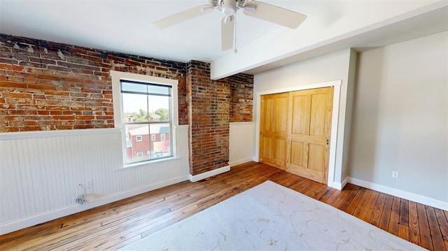1107 N 2nd St, Saint Charles, MO 63301 - unfurnished bedroom featuring wood-type flooring, a closet, brick wall, a wainscoted wall, and baseboards
