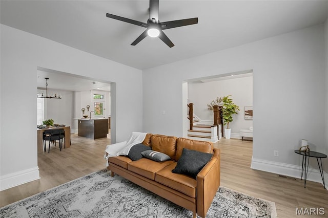 6014 Westminster Pl, Saint Louis, MO 63112 - living room featuring stairway, light wood-style flooring, a ceiling fan, and a chandelier