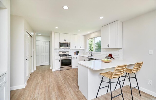 7219 Watsons Parish Dr, Ofallon, MO 63368 - kitchen with appliances with stainless steel finishes, a sink, a breakfast bar, tasteful backsplash, and light wood-style flooring