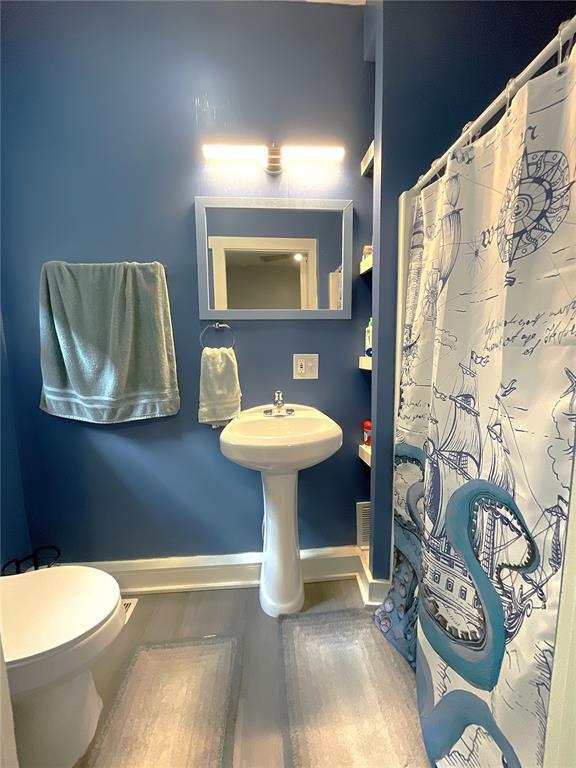 1509 Booker St, Hannibal, MO 63401 - bathroom featuring wood finished floors, baseboards, toilet, a shower with curtain, and a sink