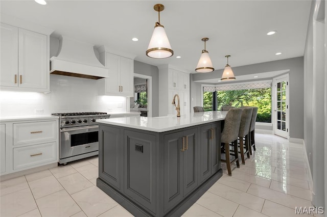 50 Lake Forest Dr, Richmond Heights, MO 63117 - kitchen featuring stainless steel stove, premium range hood, light marble finish floors, white cabinetry, and a center island with sink