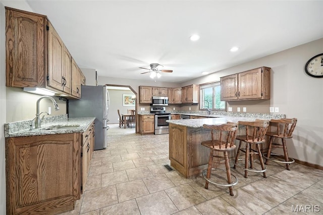 20731 Columbine Dr, Warrenton, MO 63383 - kitchen with stainless steel appliances, a peninsula, ceiling fan, brown cabinets, and a breakfast bar area