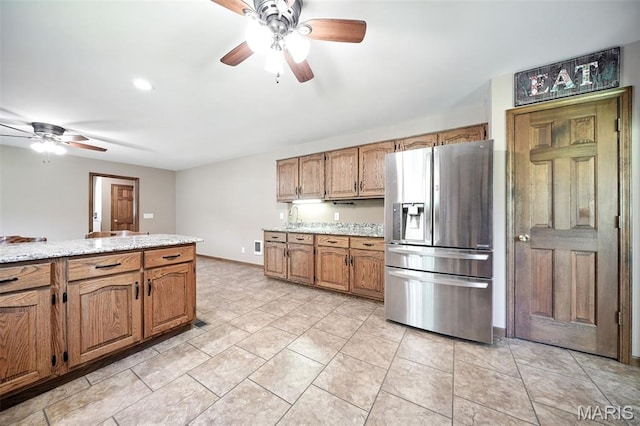 20731 Columbine Dr, Warrenton, MO 63383 - kitchen featuring stainless steel fridge, ceiling fan, brown cabinetry, light tile patterned floors, and light stone counters