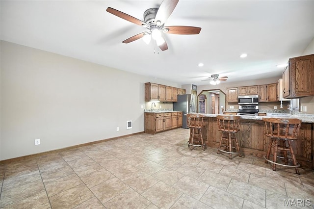 20731 Columbine Dr, Warrenton, MO 63383 - kitchen with stainless steel appliances, a ceiling fan, a peninsula, light countertops, and brown cabinetry