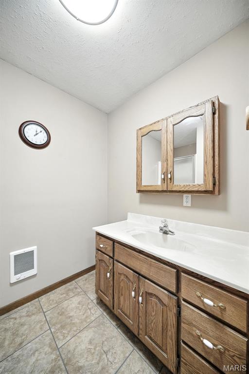 20731 Columbine Dr, Warrenton, MO 63383 - bathroom with vanity, a textured ceiling, heating unit, and tile patterned floors