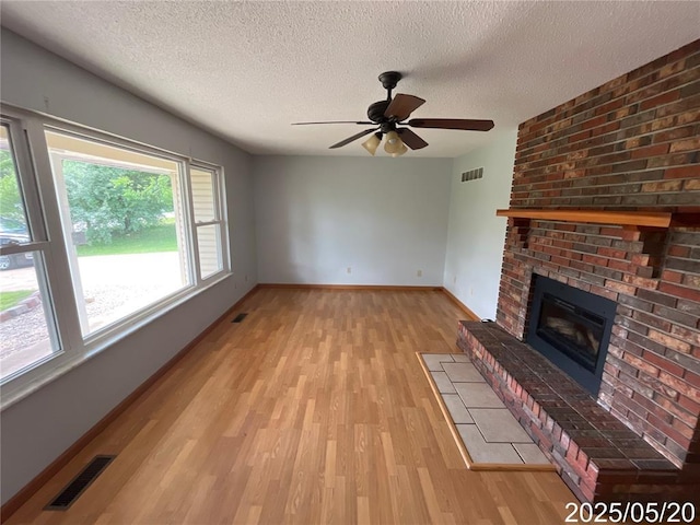 404 Glen Echo Dr, De Soto, MO 63020 - unfurnished living room featuring light wood-style floors, a textured ceiling, a brick fireplace, ceiling fan, and baseboards