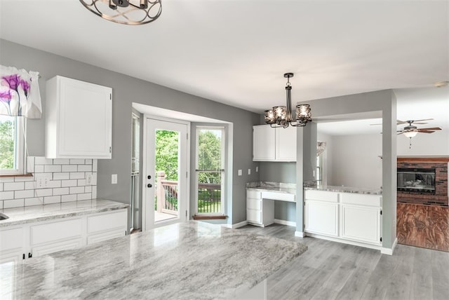 326 Merrimac Downs, Saint Peters, MO 63376 - kitchen featuring a chandelier, white cabinets, light wood-style flooring, light stone countertops, and a glass covered fireplace