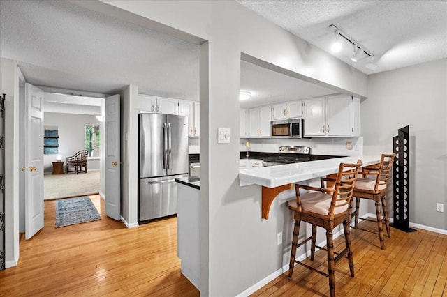 537 Colebrook Dr Unit C, Webster Groves, MO 63119 - kitchen with appliances with stainless steel finishes, a textured ceiling, light wood finished floors, a peninsula, and white cabinetry