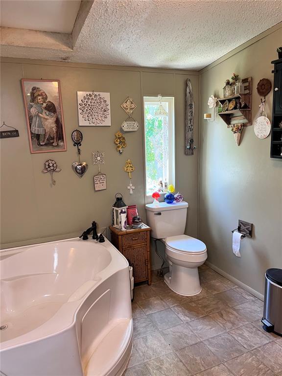 12241 Pipeline Rd, Bourbon, MO 65441 - bathroom featuring a garden tub, a textured ceiling, toilet, stone finish floors, and baseboards