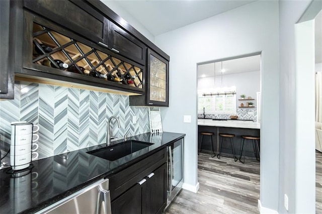 11475 Slate Cir, Rolla, MO 65401 - indoor wet bar with light wood-style floors, decorative backsplash, stainless steel dishwasher, beverage cooler, and baseboards