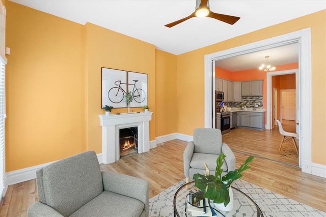 4366 Swan Ave, Saint Louis, MO 63110 - living room featuring baseboards, a warm lit fireplace, a ceiling fan, and light wood-type flooring
