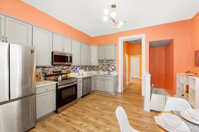 4366 Swan Ave, Saint Louis, MO 63110 - kitchen with appliances with stainless steel finishes, gray cabinetry, a sink, decorative backsplash, and a chandelier