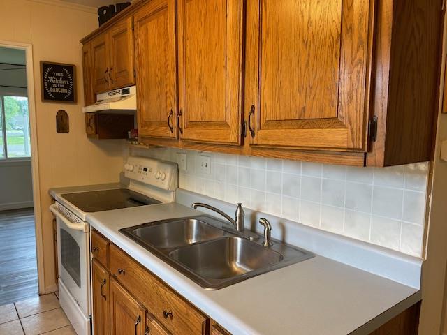 212 E N St, Benton, MO 63736 - kitchen with white range with electric stovetop, under cabinet range hood, brown cabinets, backsplash, and a sink