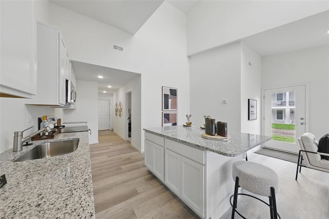 4001 Marais Temps Clair Dr, Saint Charles, MO 63304 - kitchen with a sink, a kitchen bar, white cabinets, light wood-style flooring, and a towering ceiling