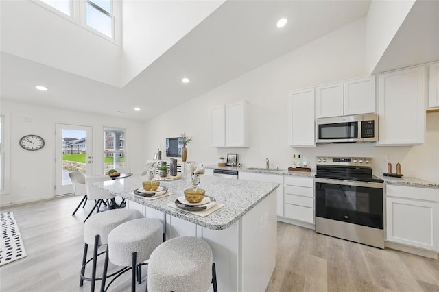 4001 Marais Temps Clair Dr, Saint Charles, MO 63304 - kitchen with stainless steel appliances, light wood-style floors, high vaulted ceiling, light stone countertops, and a kitchen bar