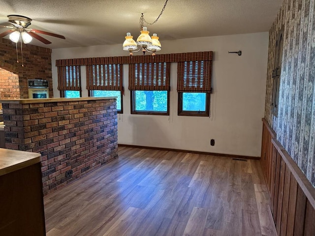 16463 Terrace Dr, Dexter, MO 63841 - unfurnished dining area with wood finished floors, a chandelier, a ceiling fan, brick wall, and a textured ceiling