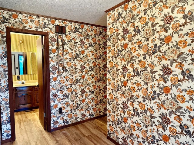 16463 Terrace Dr, Dexter, MO 63841 - empty room featuring wallpapered walls, light wood-style flooring, ornamental molding, a textured ceiling, and a sink