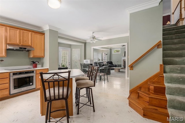 1575 Uthoff Dr, Fenton, MO 63026 - kitchen featuring stainless steel oven, under cabinet range hood, a kitchen breakfast bar, ornamental molding, and ceiling fan