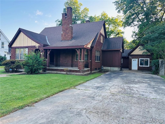 417 S Kingshighway St, Sikeston, MO 63801 - tudor-style house with brick siding, a chimney, roof with shingles, a front lawn, and a porch
