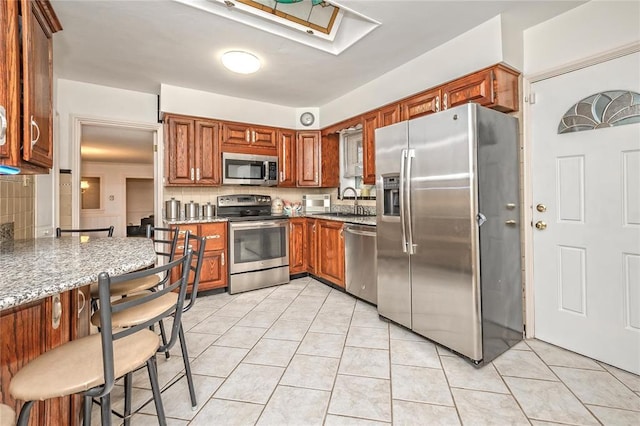 12810 Big Bend Rd, Kirkwood, MO 63122 - kitchen featuring appliances with stainless steel finishes, a sink, light tile patterned floors, and light stone counters