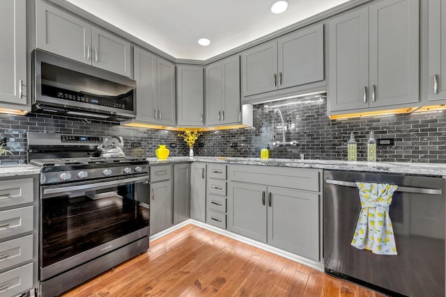 1354 Nutmeg Dr, Saint Charles, MO 63303 - kitchen featuring appliances with stainless steel finishes, gray cabinetry, light wood finished floors, and light stone countertops