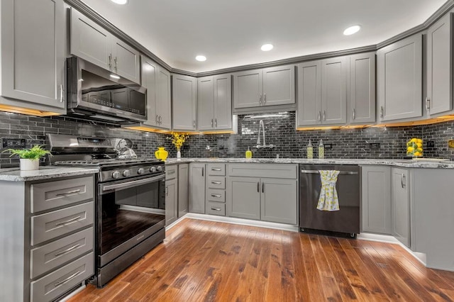 1354 Nutmeg Dr, Saint Charles, MO 63303 - kitchen with appliances with stainless steel finishes, gray cabinetry, backsplash, wood-type flooring, and light stone counters