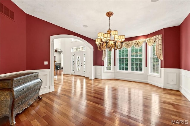 125 Park Lawn Est, Fenton, MO 63026 - unfurnished dining area featuring a chandelier, arched walkways, a wainscoted wall, hardwood / wood-style flooring, and a decorative wall