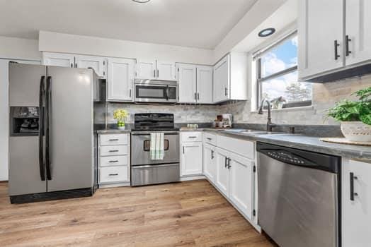 352 Della Dr, Saint Peters, MO 63376 - kitchen featuring appliances with stainless steel finishes, a sink, white cabinetry, tasteful backsplash, and light wood finished floors