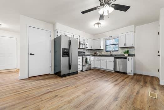 352 Della Dr, Saint Peters, MO 63376 - kitchen featuring appliances with stainless steel finishes, light wood finished floors, ceiling fan, white cabinetry, and dark countertops
