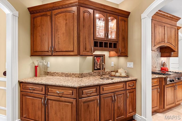 4516 Levis Ln, Godfrey, IL 62035 - kitchen with arched walkways, stainless steel gas stovetop, light stone counters, a sink, and tasteful backsplash