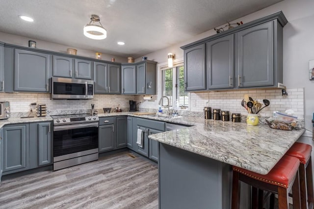 2115 Tower Rd, Lebanon, MO 65536 - kitchen featuring appliances with stainless steel finishes, a sink, a peninsula, light wood-style floors, and light stone countertops
