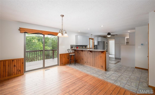 13399 S US Highway 63, Rolla, MO 65401 - kitchen featuring a peninsula, wainscoting, freestanding refrigerator, a textured ceiling, and light wood finished floors