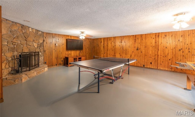 13399 S US Highway 63, Rolla, MO 65401 - game room with ceiling fan, finished concrete flooring, a textured ceiling, a stone fireplace, and wood walls