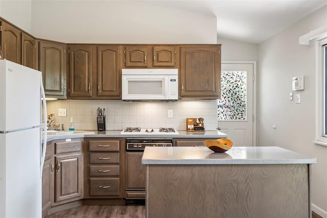 1090 Apache Dr, Florissant, MO 63033 - kitchen with white appliances, vaulted ceiling, decorative backsplash, dark wood-type flooring, and light countertops