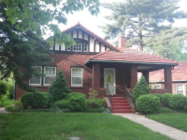 7507 Warwick Dr, Pasadena Park, MO 63121 - tudor house featuring a chimney, a front yard, a tile roof, and brick siding