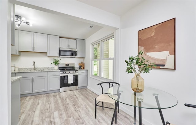 2613 Hillsboro Valley Park Rd, High Ridge, MO 63049 - kitchen featuring appliances with stainless steel finishes, light wood-style floors, light stone counters, baseboards, and a sink