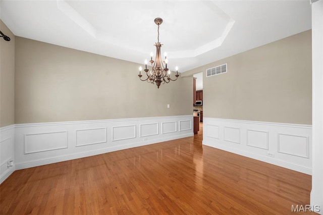 102 Riparian Dr, Ofallon, MO 63368 - empty room with a chandelier, a tray ceiling, wood finished floors, and a wainscoted wall