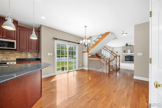 102 Riparian Dr, Ofallon, MO 63368 - kitchen with appliances with stainless steel finishes, a brick fireplace, tasteful backsplash, light wood-type flooring, and baseboards