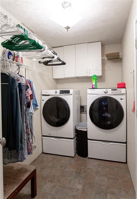 606 N Charles Ave, St James, MO 65559 - laundry area with washer and clothes dryer, a textured ceiling, stone finish flooring, and cabinet space