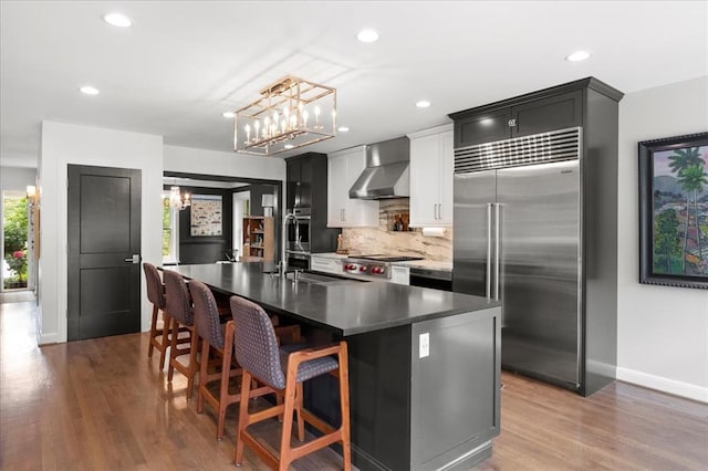 8033 Seminole Dr, Clayton, MO 63105 - kitchen with built in refrigerator, wall chimney range hood, a chandelier, a center island with sink, and tasteful backsplash