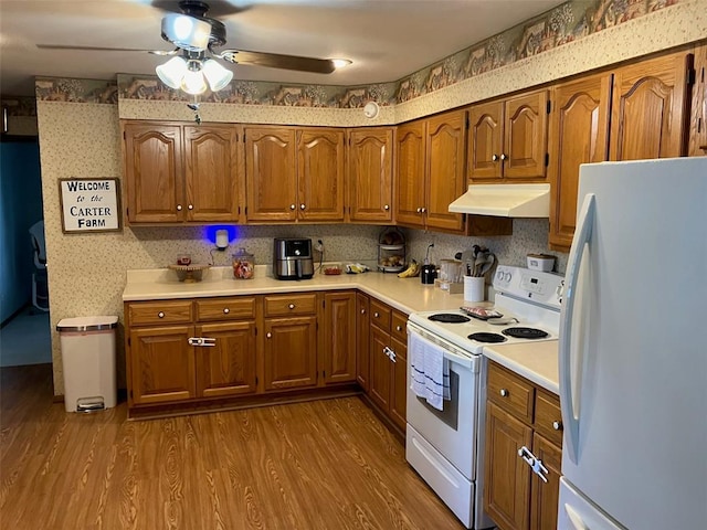 21734 Keyesport Rd, Carlyle, IL 62253 - kitchen with white appliances, under cabinet range hood, ceiling fan, brown cabinetry, and wallpapered walls