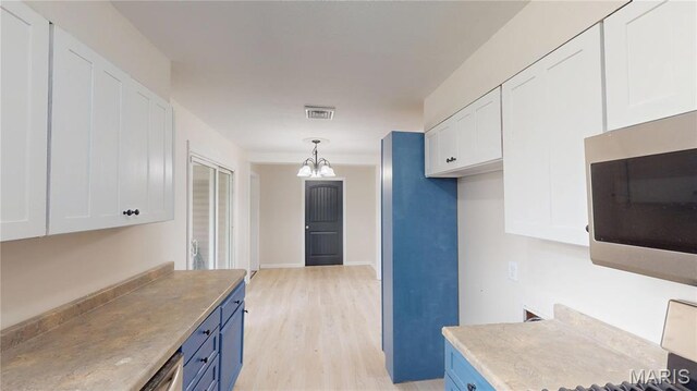 1350 Norwood Dr, Granite City, IL 62040 - kitchen with stainless steel microwave, white cabinets, light wood finished floors, blue cabinets, and a chandelier