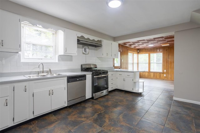 3210 Capehart Dr, Saint Louis, MO 63121 - kitchen featuring appliances with stainless steel finishes, a sink, wooden walls, a peninsula, and light countertops