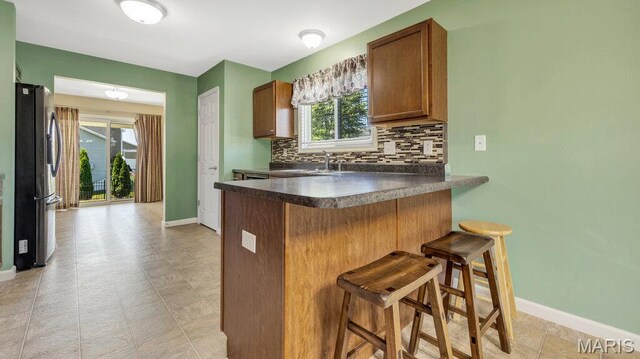 1101 Gulfstream Way, Mascoutah, IL 62258 - kitchen with freestanding refrigerator, dark countertops, a breakfast bar area, tasteful backsplash, and a peninsula