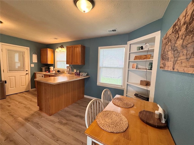711 N Lindell St, Vandalia, MO 63382 - kitchen featuring a textured ceiling, brown cabinetry, light wood-style flooring, a sink, and a peninsula