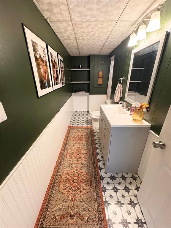 517 W Olive St, Palmyra, MO 63461 - bathroom with vanity, toilet, tile patterned floors, a decorative wall, and a wainscoted wall